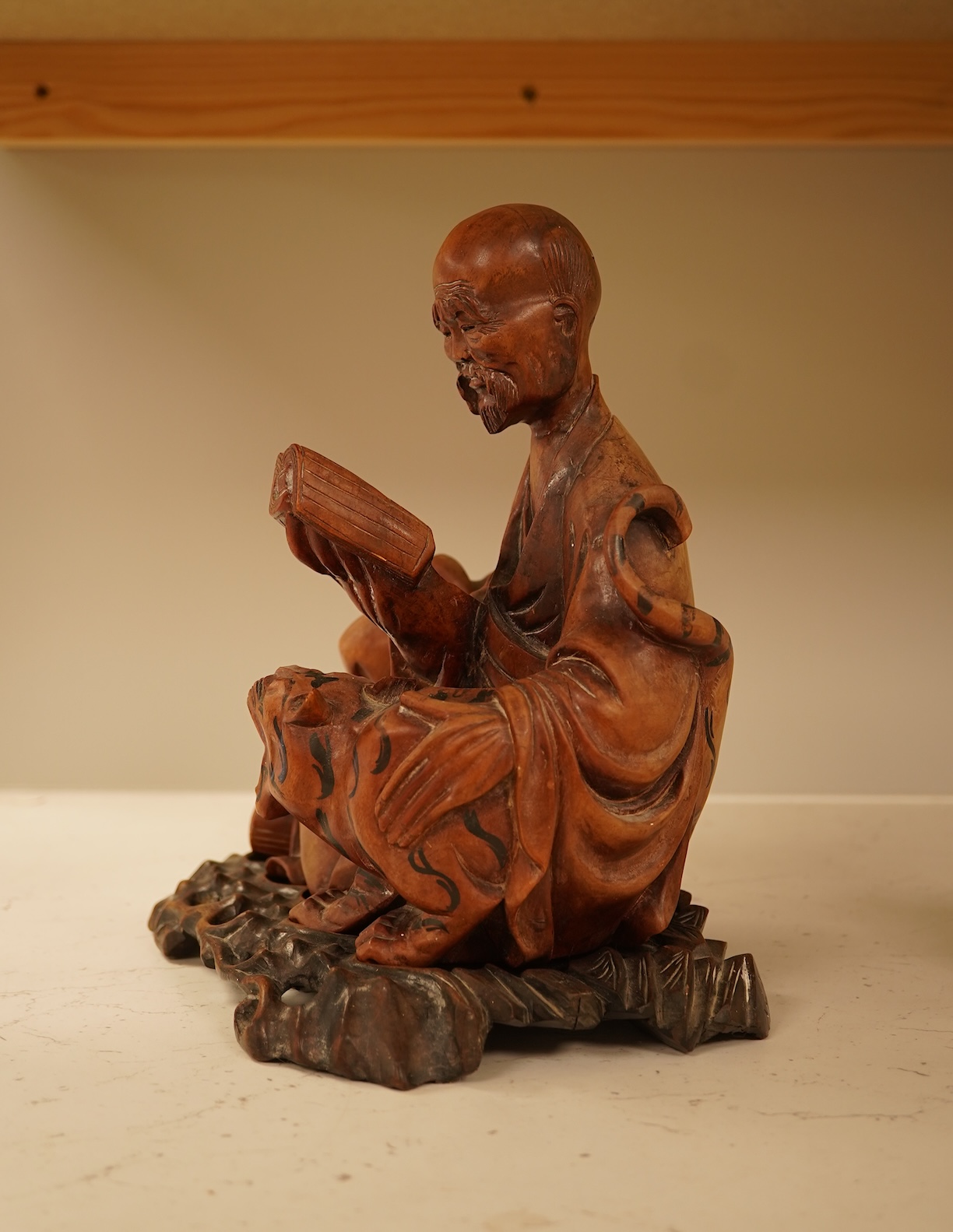 A Chinese hardwood carving of a seated luohan and tiger on hardwood stand, 24cm high including stand.